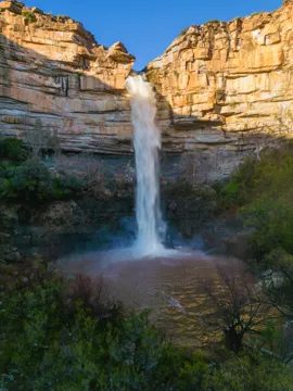 The waterfall seen from above the gorge, a white fall against sandstone cliffs